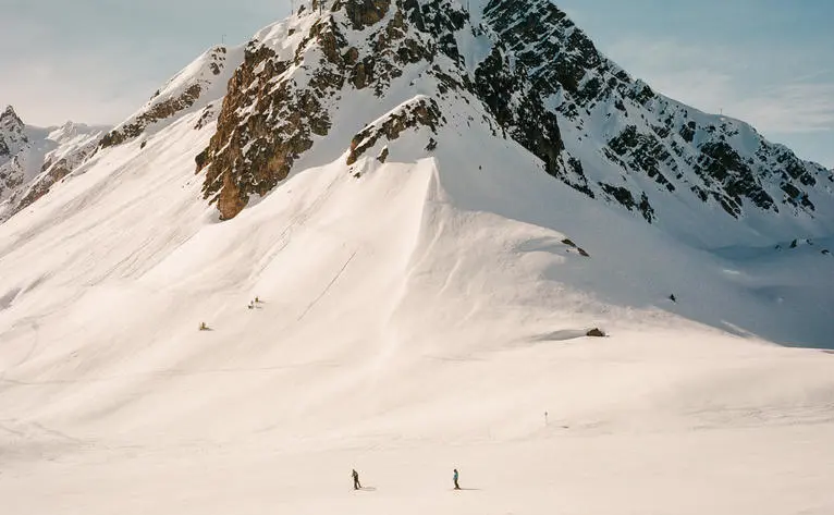 Snowy Alpine slopes at Aman Le Mélézin ski domain in France, with distant skiers on the mountainside.