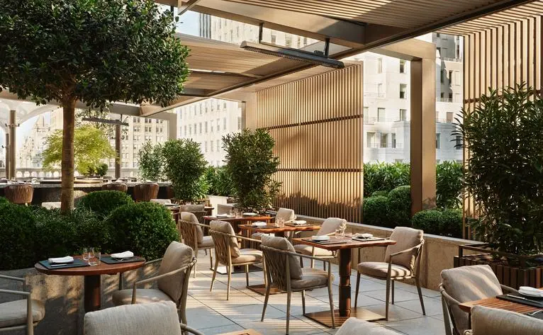 Terrazza giardino dell'Aman New York, con tavoli e sedie in legno circondate da piante verdi.