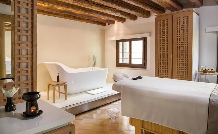 Spa treatment room at Aman Venice with twin massage beds, exposed wooden beams, and warm neutral tones.