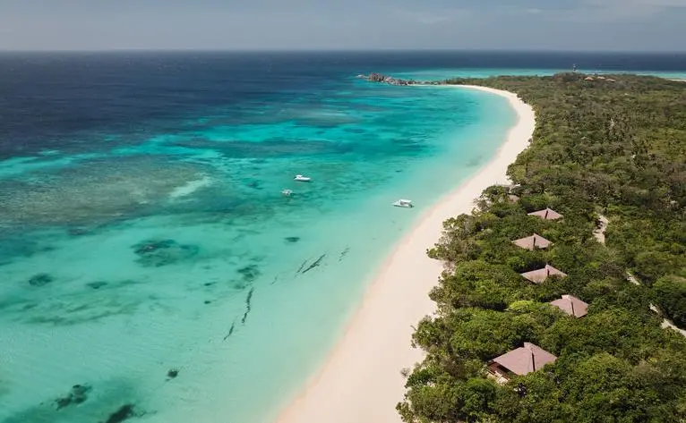 Aerial view of Amanpulo's white-sand beach and turquoise waters in the Philippines, with resort nestled among tropical vegetation.