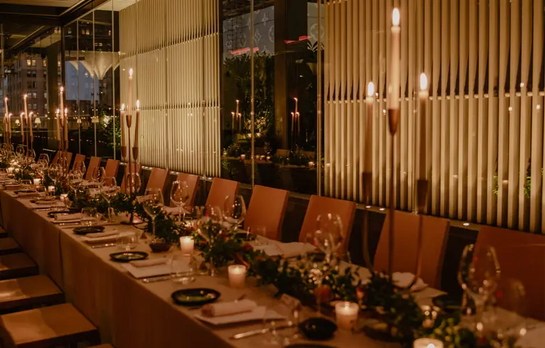 Tavolo da banchetto allestito per una celebrazione all'Aman New York hotel, con candele e decorazioni floreali.