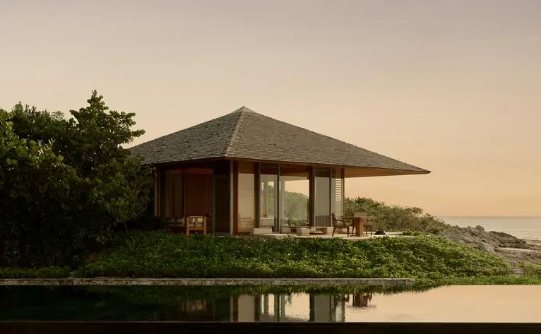 Amanyara villa pavilion at sunset, reflected in still water with landscaped grounds.
