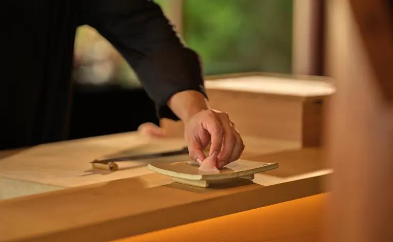 Chef's hands preparing nigiri sushi at Nama omakase counter, Amanpuri resort, Thailand.