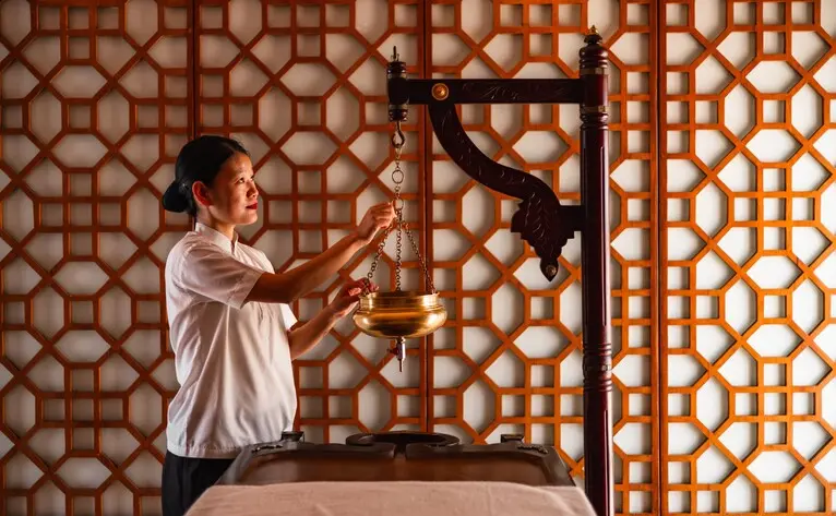 Therapist performing Shirodhara treatment at Amanbagh's spa, pouring warm oil over guest's forehead.