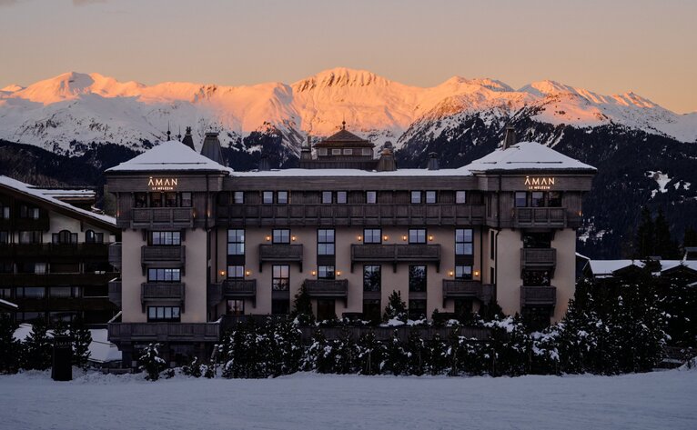 Aman Le Mélézin exterior at dusk with snow-covered Alps glowing in golden light.