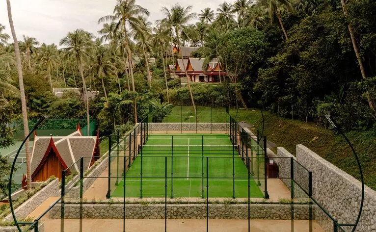Luftaufnahme des Tennisplatzes im Resort Amanpuri in Thailand, umgeben von Palmen.