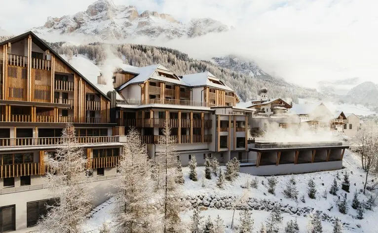 Aman Rosa Alpina exterior with snow-covered Alpine peaks rising behind traditional wooden architecture.