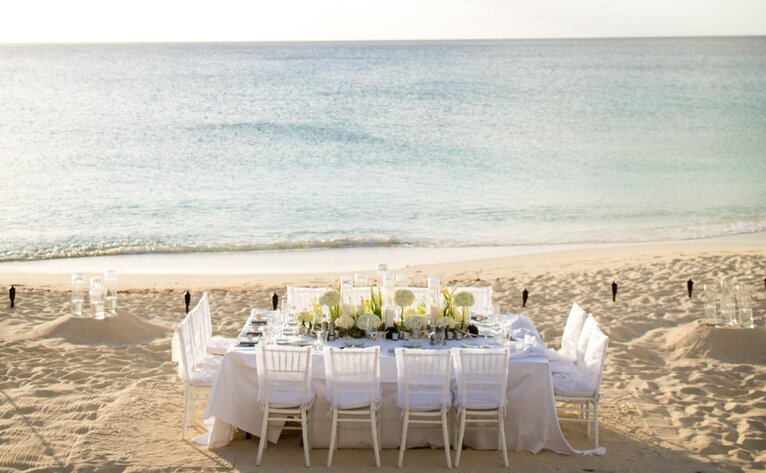 Amanyara beach dinner setup with white-draped table and chairs on sand at sunset, Turks and Caicos.