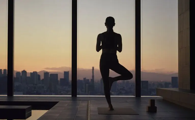 Silhouetted figure practising yoga at Aman Tokyo with Tokyo skyline at sunset visible through floor-to-ceiling windows.