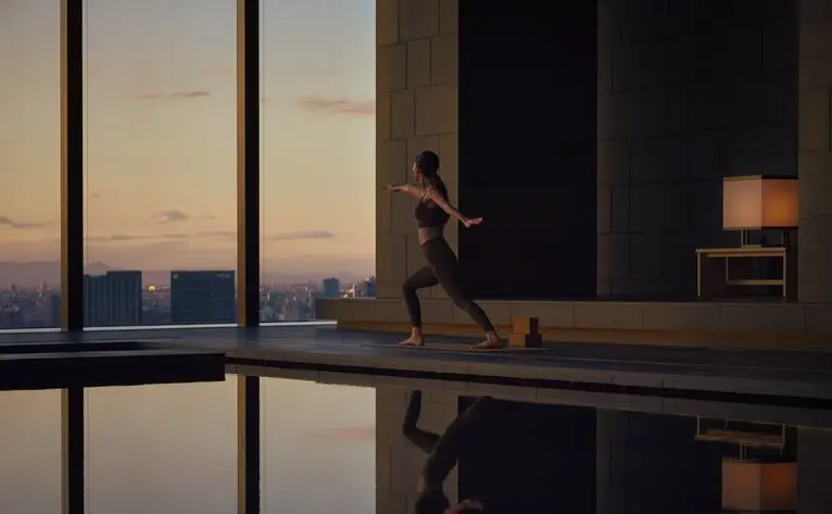 Silhouette of a person practising yoga at Aman Tokyo, overlooking the city at dusk.