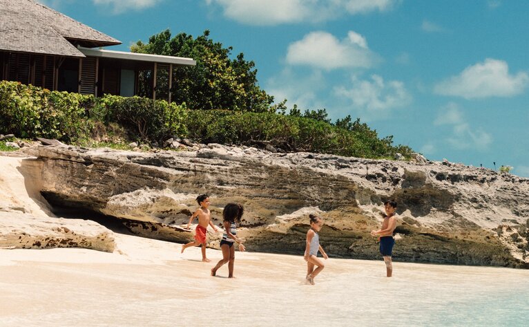 Children playing on a white sand beach below limestone cliffs at Amanyara, Turks and Caicos.