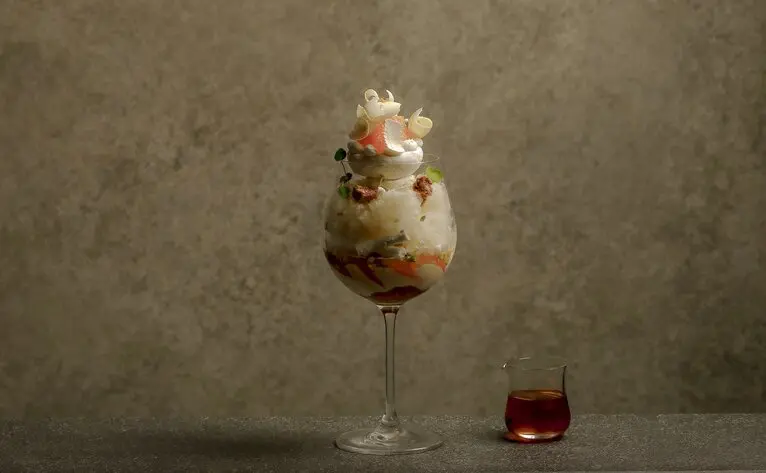 Citrus parfait served in a tall glass at Aman Tokyo's lounge, with a small glass of red liquid beside it.