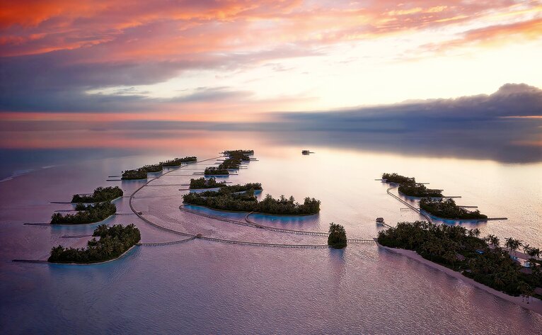 Aerial view of Aman Residences in the Maldives at sunset, with overwater villas scattered across calm turquoise waters.