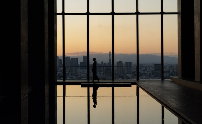 Silhouette of a person standing at a window overlooking Tokyo's skyline at dusk, Aman Tokyo.