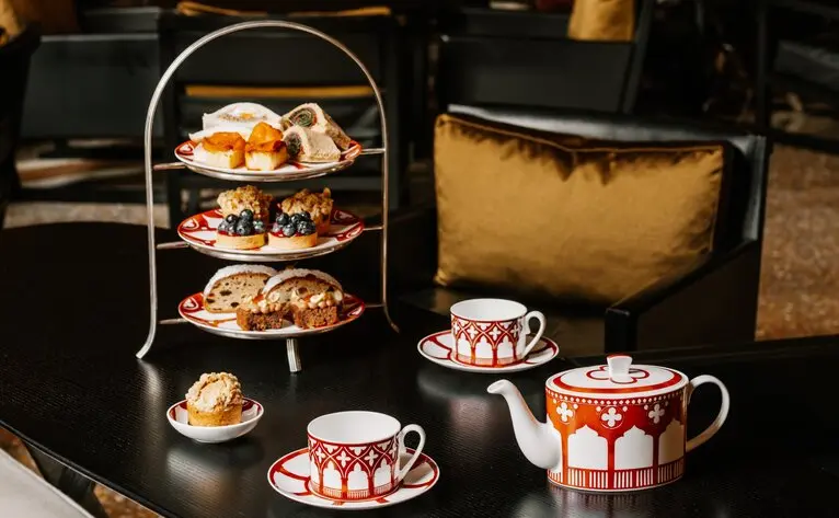 Afternoon tea service at Aman Venice hotel, with tiered stand of pastries, teapot and cups on dark table.