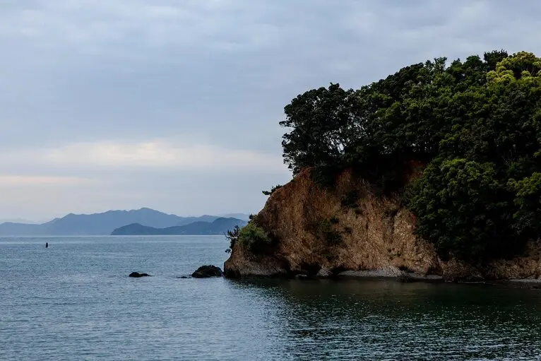 Sunset cruise waters near Amanemu resort, Japan, with rocky coastline and distant mountains.