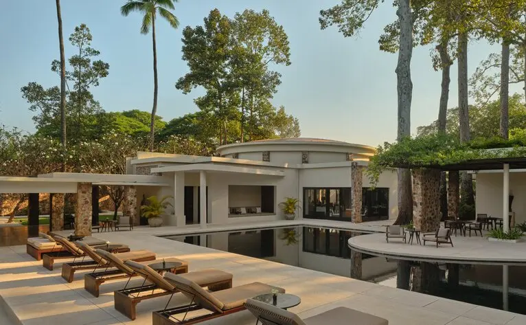 Amansara's main pool area with dining room and loungers beneath tall palms, Cambodia.