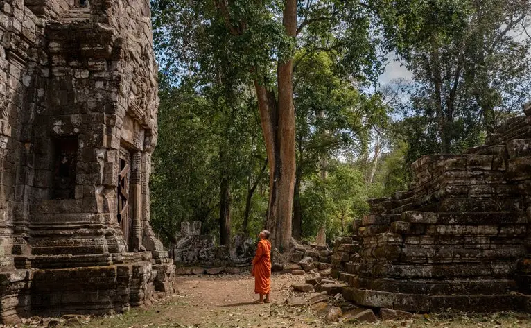 Buddhist monk walking amongst ancient temple ruins at Angkor, Cambodia.