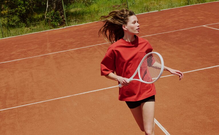 Young player in red shirt practising on clay tennis court at Amanjena.
