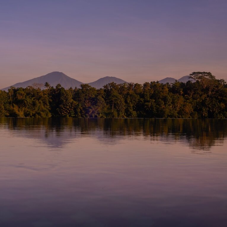Dawn light over Amandari's riverside setting with volcanic peaks reflected in still water.