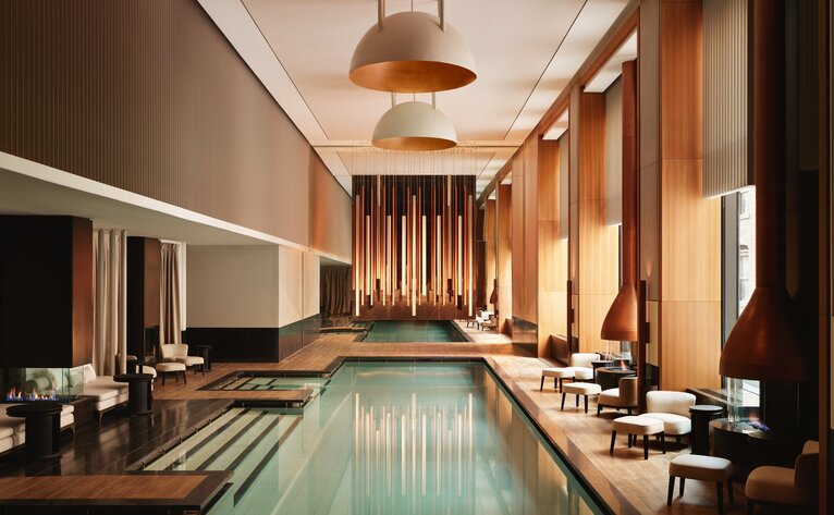 Spa pool at Aman New York, lined with wooden columns and warm lighting.