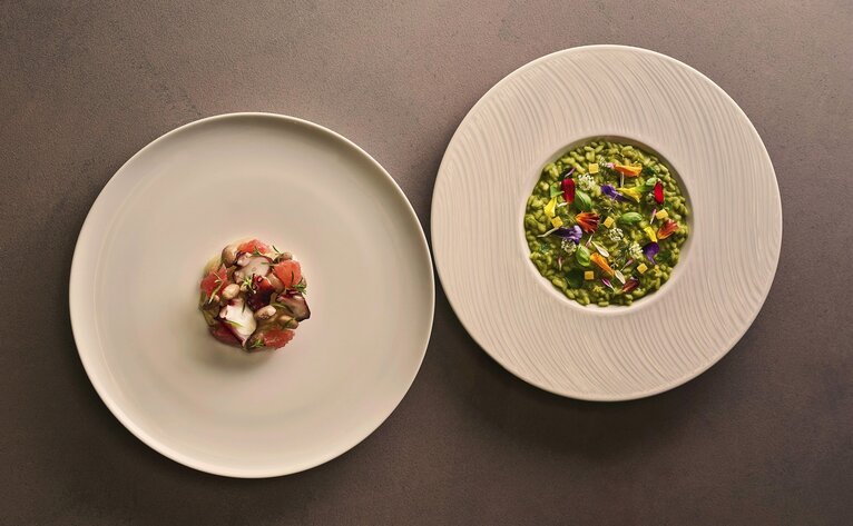 Two plated dishes at Aman Tokyo's dining venue: one with a small composed appetiser, the other with a vibrant green vegetable preparation.