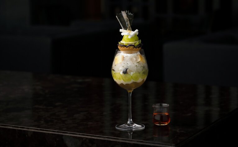 Shine Muscat cocktail at Aman Tokyo's lounge, garnished with fruit and served in a tall glass.