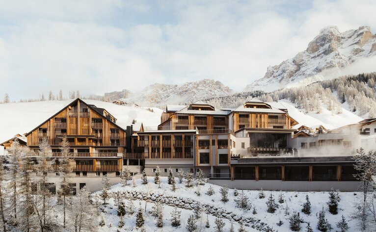 Aman Rosa Alpina resort exterior in winter, with wooden chalet architecture set against snow-covered alpine peaks.