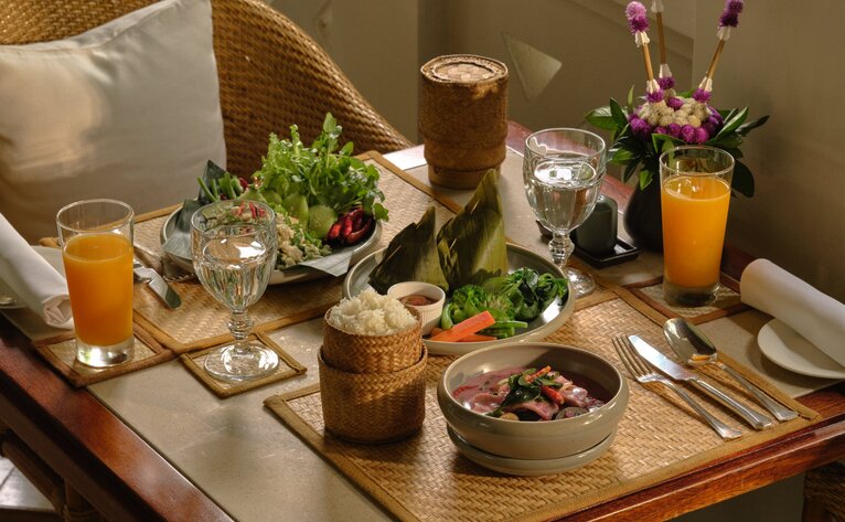 Amantaka dining table set for sharing style Lao Old Court menu with fresh ingredients and beverages.