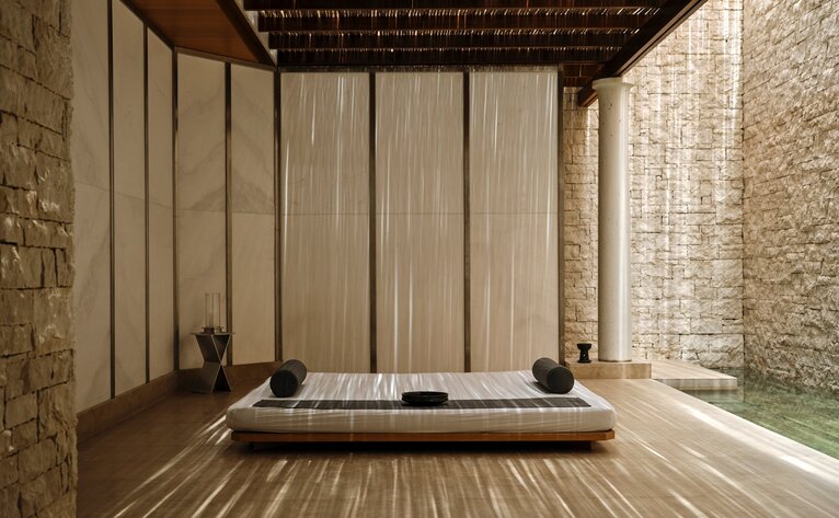 Spa treatment room at Amanzoe with wooden platform bed, draped curtains, and stone walls.