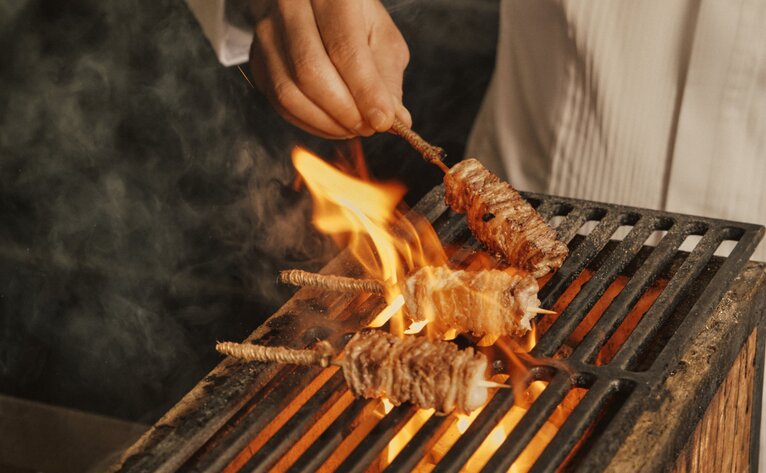 Meat skewer being grilled over flames at Aman Venice's Palazzo Kitchen Table yakiniku grill.