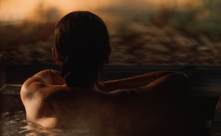 Silhouetted figure soaking in a private onsen at Amanemu, Japan at sunset.