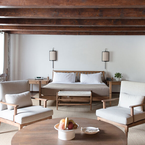 Deluxe cottage bedroom at Aman Sveti Stefan with wooden beams, neutral furnishings, and seated area overlooking Montenegro's coast.