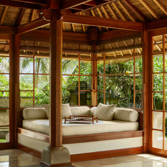 Duplex Pool Suite living area at Amandari with four-poster bed, wooden beamed ceiling and garden views through glass doors.
