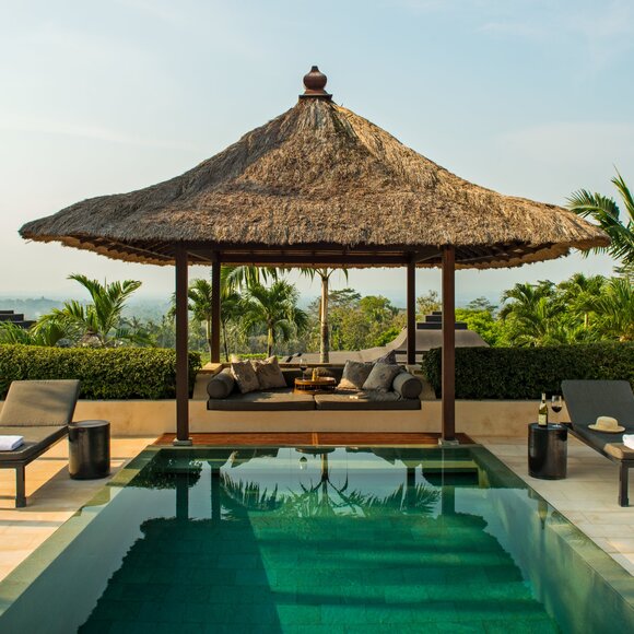 Amanjiwo's pool pavilion overlooks a reflecting pool with traditional pitched roof and wooden loungers.