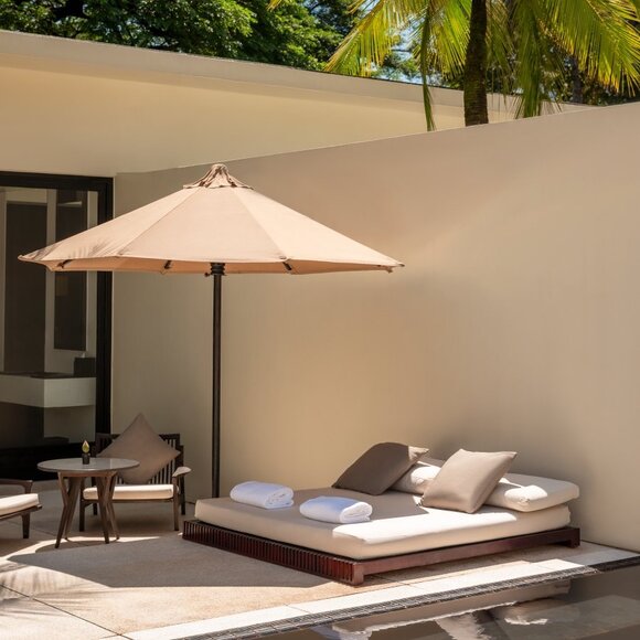 Amansara pool suite exterior with shaded daybed and umbrella against cream wall.