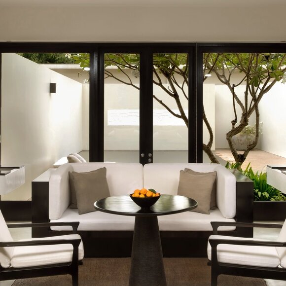 Pool Suite seating area at Amansara, Cambodia, with floor-to-ceiling windows overlooking tropical gardens.