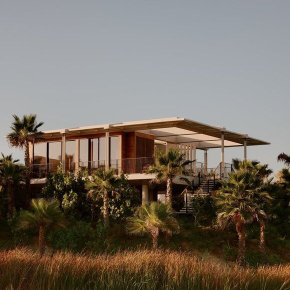 Amanvari casita with extended canopy sheltering the structure, surrounded by desert landscape and palm trees at golden hour.
