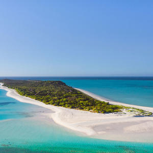 Aerial view of Amanpulo's island with white sand beach, turquoise waters and forested interior.