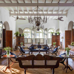 Amangalla's light-filled lounge with high ceilings, ornate chandelier, and period furnishings arranged around a central seating area.