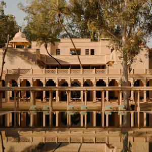 Amanbagh's main building reflected in the pool, with arched colonnades and warm stone architecture framed by trees.