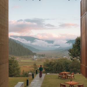 Outdoor dining terrace at Amankora's Gangtey Lodge overlooking a misty valley and forested mountains at dusk.