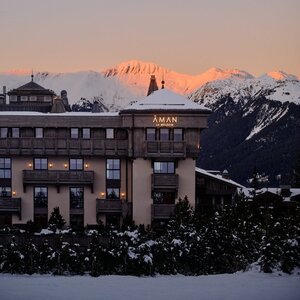Aman Le Mélézin exterior at dusk, with snow-covered peaks glowing in alpenglow light beyond.