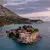 Aman Sveti Stefan's islet property with stone buildings surrounded by Adriatic waters and coastal mountains at dusk.