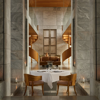Private dining room at Amanzoe with marble columns, wooden chairs, and a central table set for two.