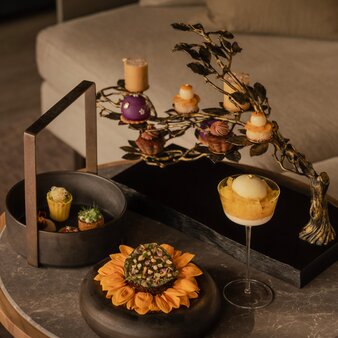 Afternoon tea service at Aman Nai Lert Bangkok with golden pastries and autumn floral arrangement on slate table.