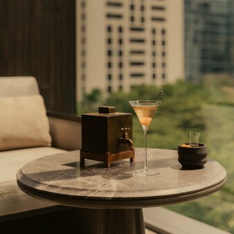 Cocktail served on marble table at Aman Nai Lert Bangkok, with city views beyond.