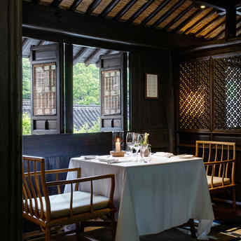 法云安缦度假村的餐厅内，白色桌布覆盖餐桌，木质椅子围绕，大窗户映照自然光线。