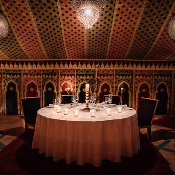 Candlelit round dining table set for an intimate meal in Amanjena's ornately decorated Caïdal Tent, Morocco.