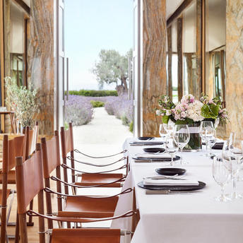 Dining table set for an event at Amanzoe, with views towards the Aegean Sea framed by open doors.